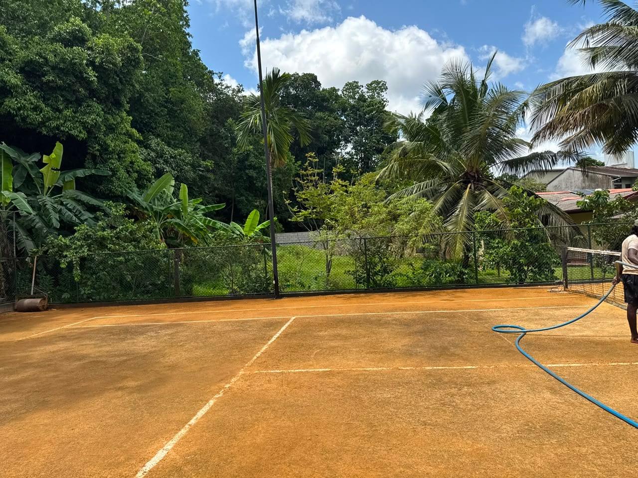 Clay court being watered before the sponsorship, with bare fencing behind